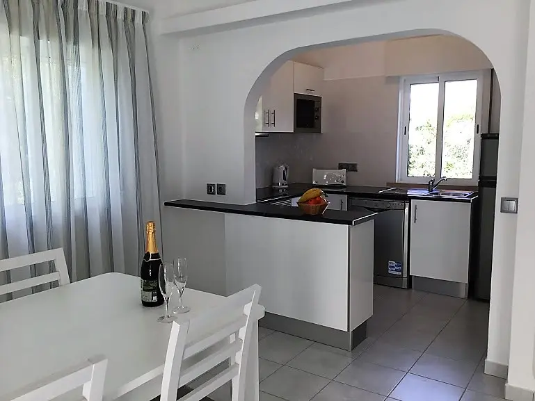 apartamentos férias Vilamoura com cozinha equipada mesa branca com cadeira e cozinha ao fundo com armários brancos