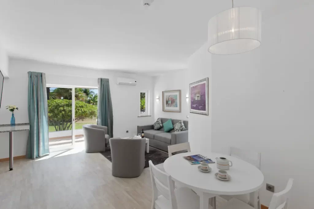 White dining table with white chairs. Grey sofas in the background overlooking terrace