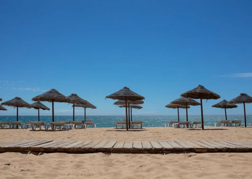 family-holidays-vilamoura-praia-de-quarteira-beach rows of straw beach umbrellas at Praia de Quarteira beach